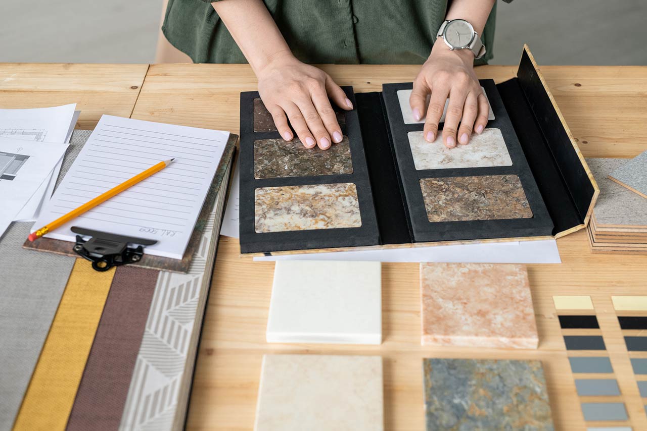 Hands of designer on samples of marble tile surrounded by wallpaper patterns during work over new project or order of client
