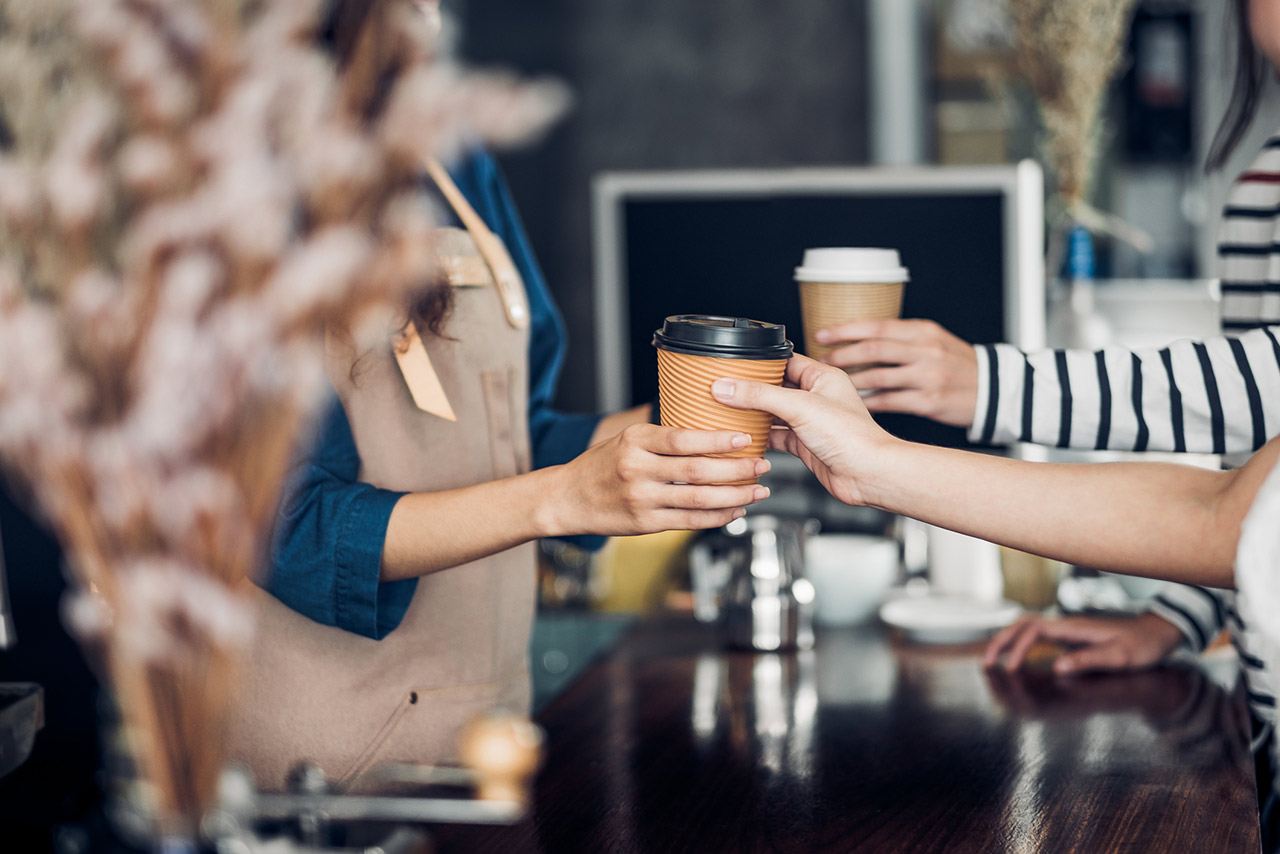 Barista served take away hot coffee cup to customer at counter bar in cafe restaurant